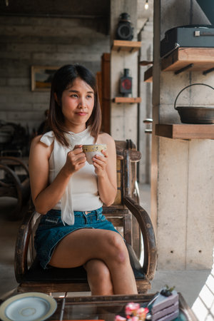 A young woman sits in a stylish cafe, savoring a cup of coffee, surrounded by modern decor and natural light.の写真素材