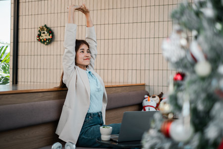 Professional woman stretching in a festive office setting with Christmas decorations and a laptop.の写真素材