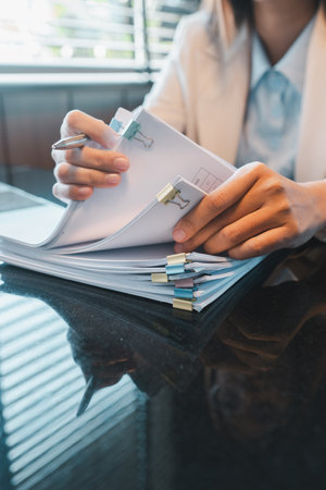 Close-up of a professional organizing documents with binder clips at a modern office desk, illuminated by natural light.の写真素材