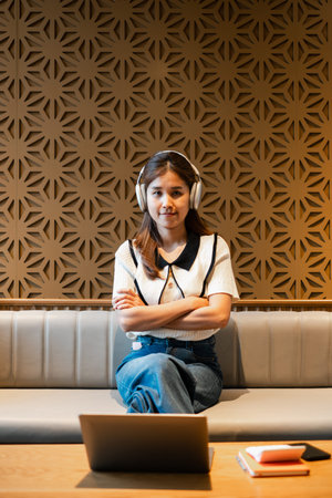 Woman wearing headphones sitting on a sofa with a laptop, set against a modern geometric wall...
