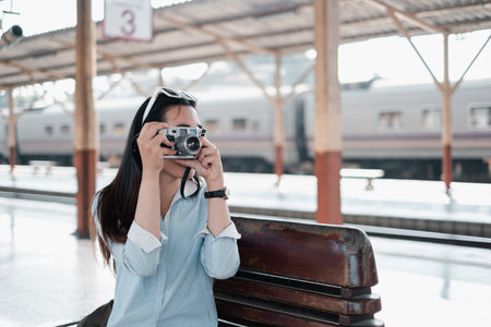 Young woman using a vintage camera at a train station, capturing moments on a sunny day.の写真素材