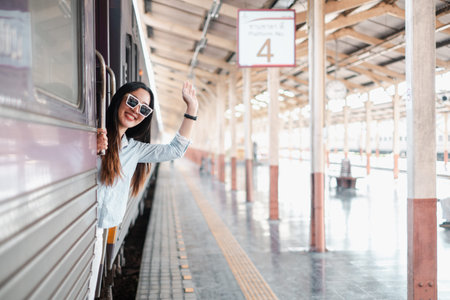 A woman waves from a train at a station with a wooden roof, capturing the joy of travel and...