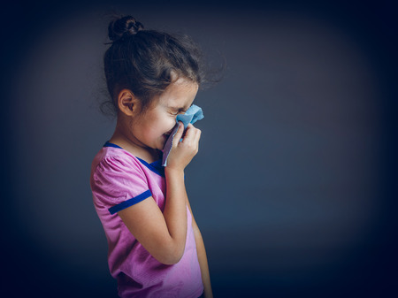 Teenage girl suffers runny nose handkerchief on a gray backgrounの写真素材