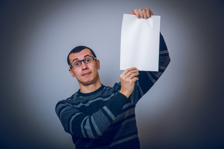 European-looking male holding a white sheet of paper on grayの写真素材