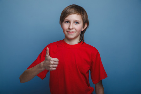 European-looking boy of ten years thumbs up on gray backgroundの写真素材