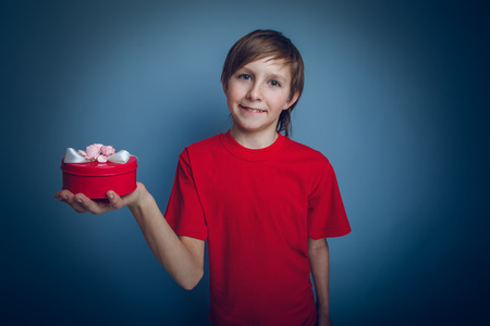 Teenage boy holding a European-looking red box in hand on gray bの写真素材