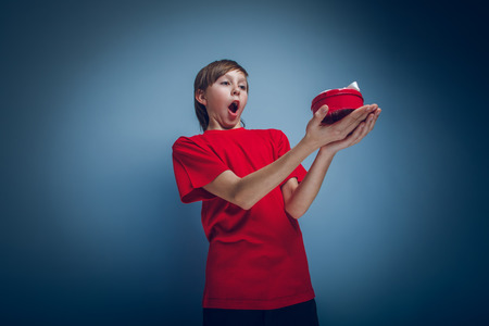 Teenage boy holding a European-looking red box on a gray backgroの写真素材