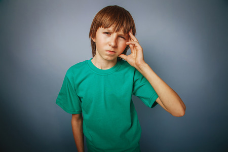 European-looking boy of ten years headache, migraine on a gray bの写真素材