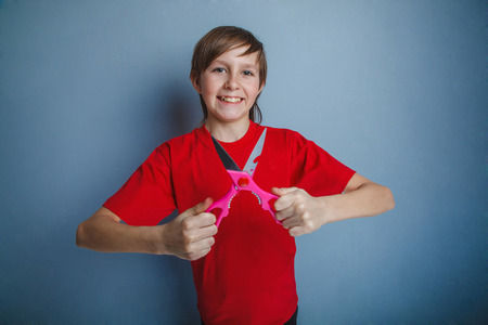 Boy, teenager, twelve years in the red shirt is holding a pair of scissorsの写真素材