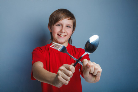 Teenager boy in red shirt twelve years holding a spoon and fork, breakfast hungerの写真素材