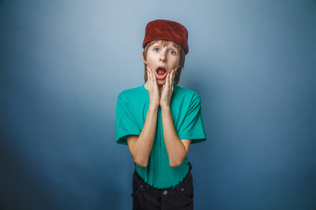 Muslim boy of ten years, skullcap, surprise, his hands on his face on a gray backgroundの写真素材