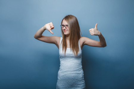 European-looking girl of twenty years thumbs up, thumbs down on a gray backgroundの写真素材