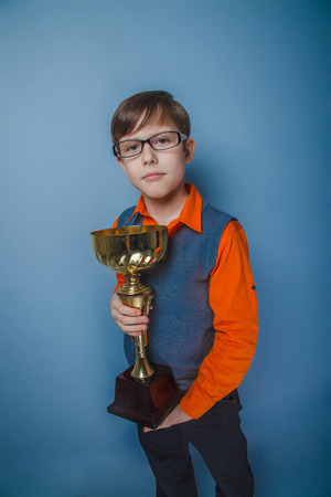 European-looking boy of ten years in glasses reward, pleasure, cup on a gray の写真素材