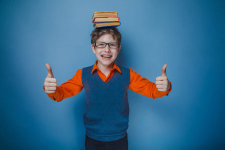 European-looking boy of ten years in glasses with books on her head, thumbs up on a gray 