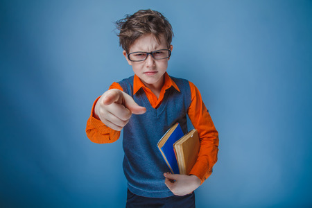 teenager boy brown hair European appearance in retro clothes with books in glasses shows finger forward on a gray backgroundの写真素材