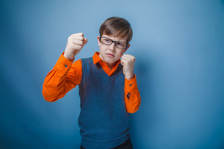teenager boy of twelve European appearance in brown hair retro clothes clenched his hands into fists on a gray background, rage, fightの写真素材