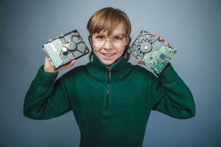 European-looking boy of ten years in glasses holding a hard drive on a gray background