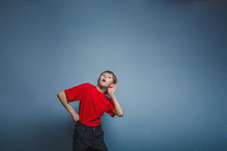 Boy, teenager, twelve years in a red shirt holding his ear hand, overhears