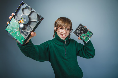 European appearance teenager boy with big glasses in a long green jumper holds a computers hard disks on a gray background, retro, computer technicianの写真素材