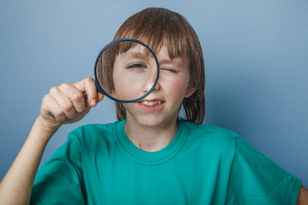 Boy, teenager, twelve years in a green t-shirt, looking through a magnifying glass with one eyeの写真素材