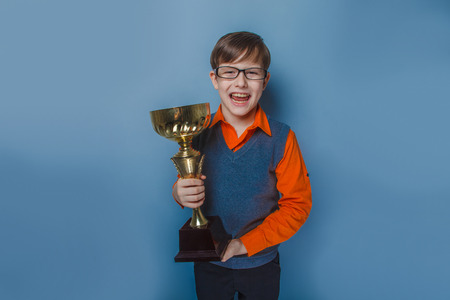 European-looking  boy of  ten years  in glasses holding a cup, award joy on a blue backgroundの写真素材