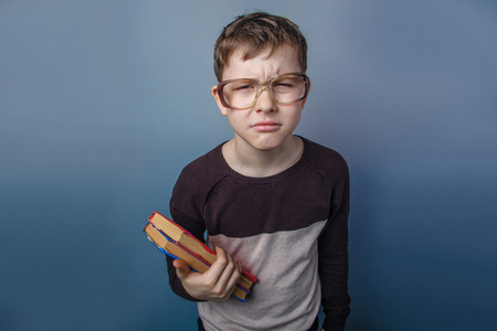 European-looking boy of ten years  in  glasses reading  a book on  a gray backgroundの写真素材