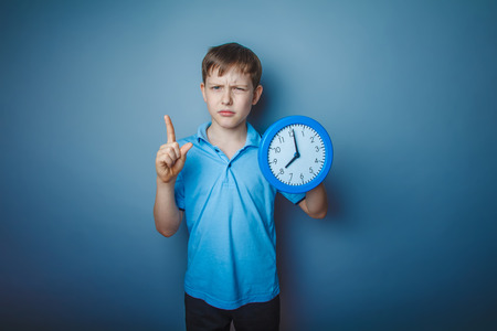 teenager boy brown European appearance holds a clock showing thuの写真素材