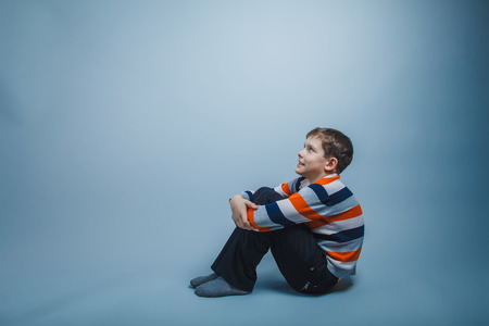 Boy teenager European appearance sitting on the floor and lookinの写真素材