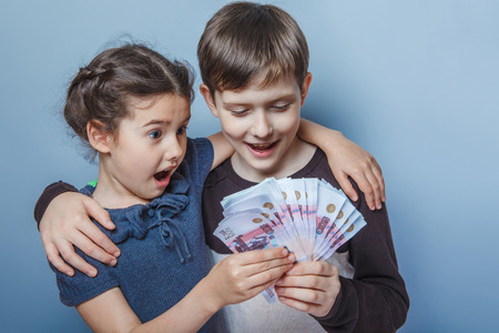teenage boy and girl holding money bills in his hands on a grayの写真素材