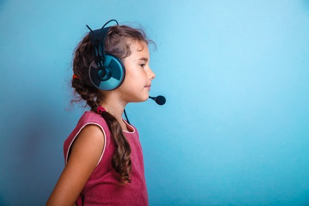 Teen girl child in headphones with a microphone sideways in profile on a blue background photo studioの写真素材