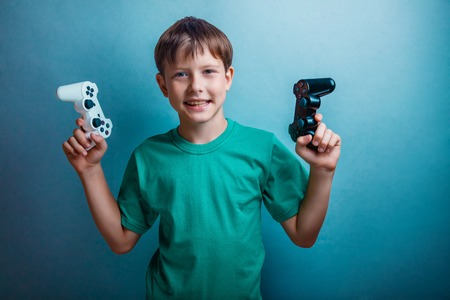 Teenage boy holding a game joystick on a blue background studio photoの写真素材