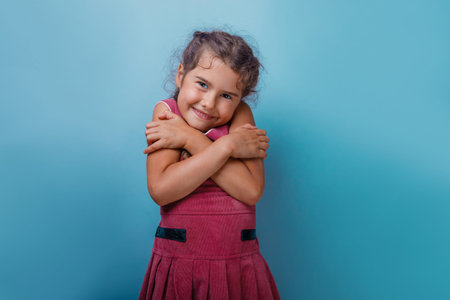 Girl European appearance decade hugging herself on a blue  backgroundの写真素材