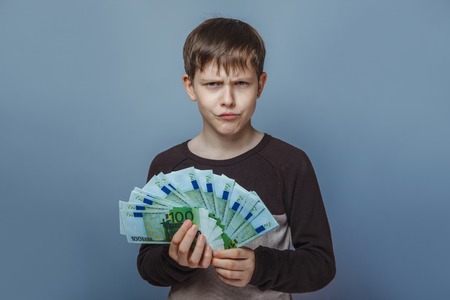 Boy teenager European appearance ten years  holding a  wad of money  on a gray  backgroundの写真素材