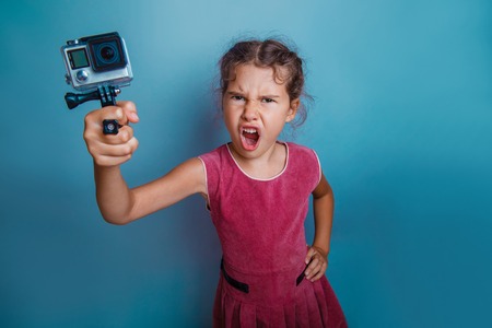 Girl child holding a camera in his hand shooter opened her mouth shouts gray  backgroundの写真素材