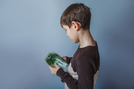 Boy teenager ten years  European appearance holding a wad  of money on a gray  background