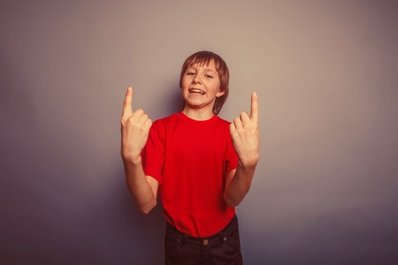 boy teenager European appearance in a red shirt shows the number two fingers on a gray background retroの写真素材
