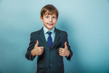 Teen boy businessman in a suit showing gesture yes thumbs up on a blue background photo studio