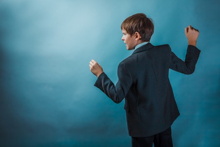 Teen boy clenched his fists fights businessman standing in profile against the background of the photo studioの写真素材