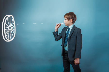 Teen boy businessman throwing darts at a target dart on a blue background studioの写真素材