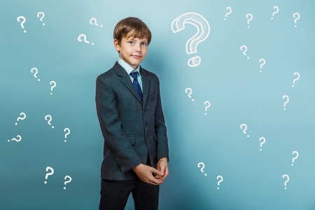 a boy of twelve European appearance in a suit holding a blank sheet on a  gray  backgroundの写真素材