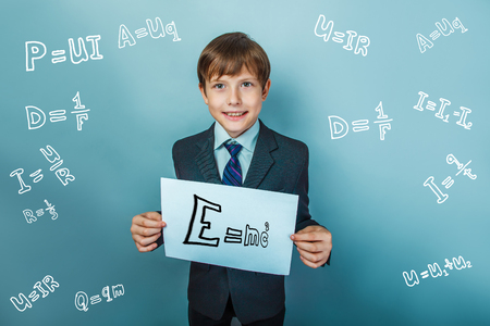 a boy of twelve European appearance in a suit holding a blank sheet on a  gray  backgroundの写真素材