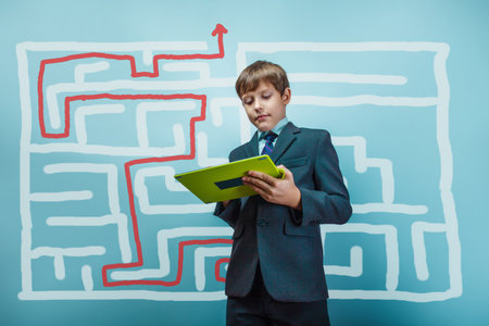 a boy of twelve European appearance in a suit holding a blank sheet on a  gray  backgroundの写真素材
