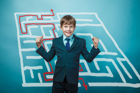 a boy of twelve European appearance in a suit holding a blank sheet on a  gray  backgroundの写真素材