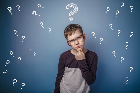 a boy of twelve European appearance in a suit holding a blank sheet on a  gray  backgroundの写真素材