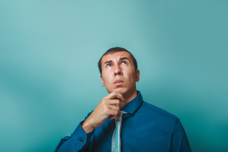 a man of European appearance thirty years thinking hand on  chin on a  gray  backgroundの写真素材