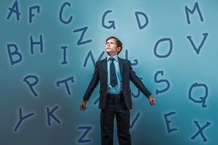 a boy of twelve European appearance in a suit holding a blank sheet on a  gray  backgroundの写真素材