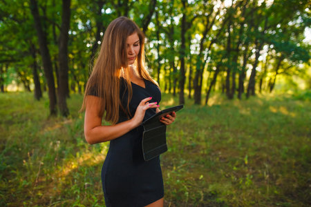 woman girl working on a tablet in the woods on the nature of the blonde in a black dressの写真素材