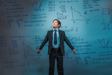 a boy of twelve European appearance in a suit holding a blank sheet on a  gray  backgroundの写真素材