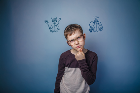 a boy of twelve European appearance in a suit holding a blank sheet on a  gray  backgroundの写真素材