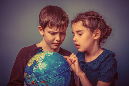 Teenage boy with a girl looking at a globe girl opened her mouth on a gray  background retroの写真素材